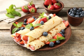 Tasty crepes with berries, cream and mint on wooden table, closeup
