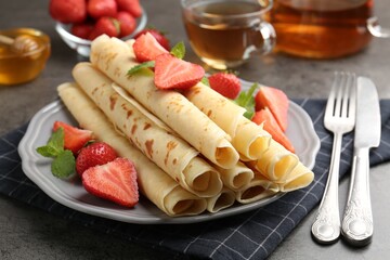 Tasty crepes with strawberries and mint on grey table, closeup