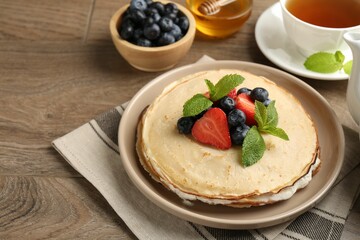 Delicious crepes with berries, cream, mint, honey and tea on wooden table, closeup