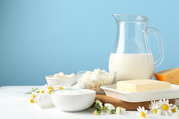 Fresh dairy products and flowers on white wooden table against light blue background