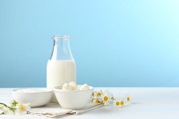 Fresh dairy products and flowers on white wooden table against light blue background. Space for text