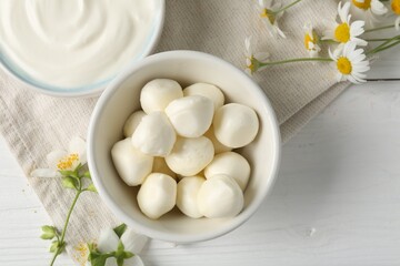 Fresh mozzarella cheese, sour cream in bowls and flowers on white wooden table, flat lay. Dairy products