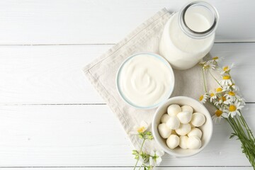 Fresh dairy products and flowers on white wooden table, flat lay. Space for text