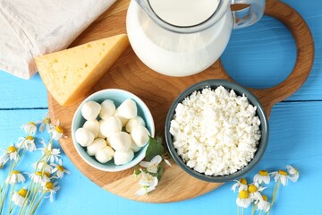 Different fresh dairy products and flowers on light blue wooden table, flat lay