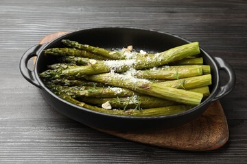 Tasty cooked asparagus served with parmesan on black wooden table, closeup