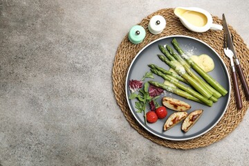 Tasty cooked asparagus served with baked potatoes, tomatoes and sauce on grey table, flat lay....