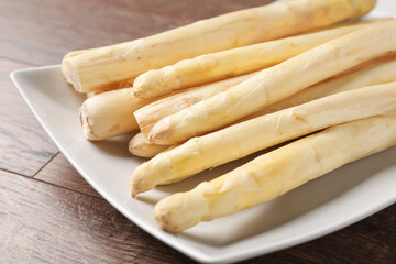 Raw white asparagus spears on wooden table, closeup