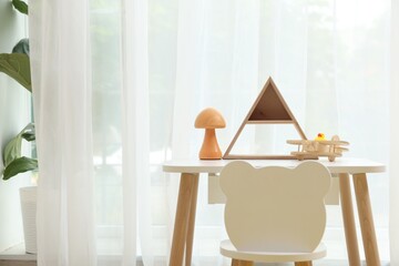 Small table, chair and decor near window in stylish playroom. Interior design
