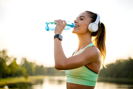 Athletic woman drinking water wearing headphones outdoors bottle