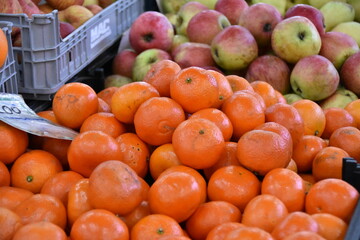 A vibrant fruit market display with fresh, shiny tangerines in the foreground and a mix of red and...