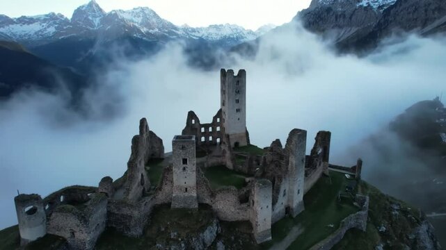 Ancient stone castle ruins perched dramatically on a misty mountain peak surrounded by low lying clouds and snow capped peaks