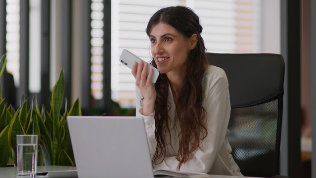 Smiling business woman Caucasian girl talk loudspeaker mobile phone speakerphone gadget record voice mail audio message send cellphone female happy businesswoman employee chatting voicemail in office