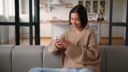 Hispanic woman happy girl lady female user at home kitchen browsing mobile phone app shopping...
