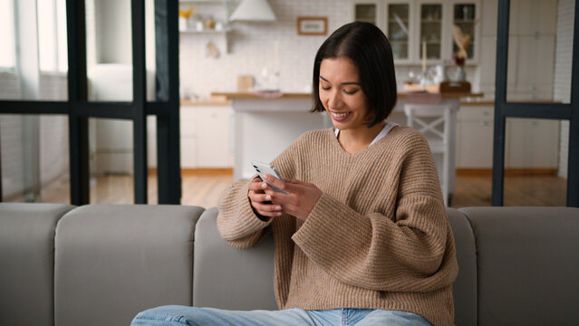 Hispanic woman happy girl lady female user at home kitchen browsing mobile phone app shopping online reading social media laugh smile smartphone addicted shopper buyer using internet order delivery