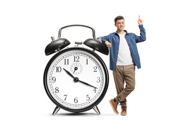 Full length portrait of a guy leaning on a big alarm clock and pointing up