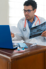 Vertical shot of professional doctor reviews a dental x-ray image and reading medical prescription while working on a laptop in an organized medical office