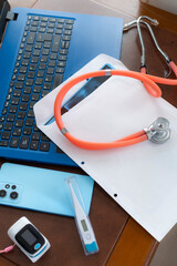 A stethoscope, digital thermometer, smartphone, and laptop on a desk represent modern healthcare technology integration.