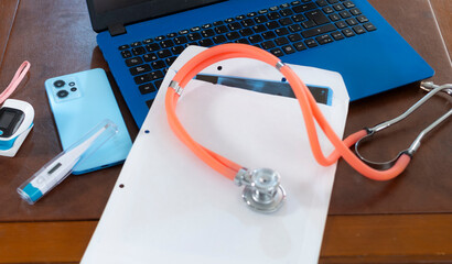 A stethoscope, digital thermometer, smartphone, and laptop on a desk represent modern healthcare technology integration.
