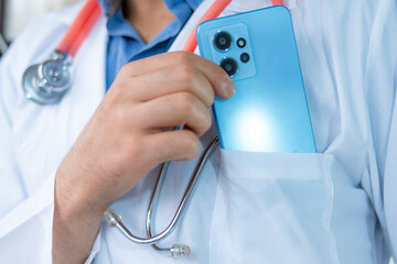 A healthcare professional wearing white coat and stethoscope taking his phone from coat,...