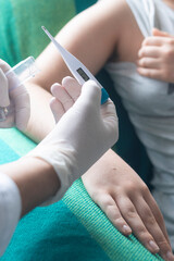 Vertical shot of healthcare professional measuring an individual's temperature using a digital thermometer, emphasizing health, diagnosis, and patient care, focus on foreground.