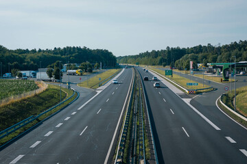 clean, modern highway with light traffic, surrounded by green forests and fields. There s a service...
