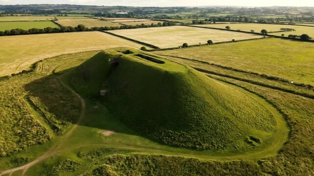 Aerial view of a motte and bailey castle earthwork on a grassy hill in the countryside