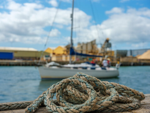 Old mooring rope on the dock with sailboat in background &ndash; summer day at the marina