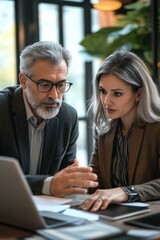 Team of diverse partners mature Latin business man and European business woman discussing project on laptop sitting at table in office. Two colleagues of professional business people working together.
