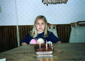 Angsty tween girl and a birthday cake at the kitchen table, circa 1992. 90s children. Image is a vintage scan and may have imperfections
