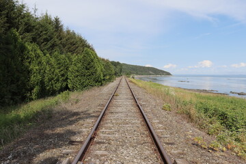 Obraz premium Railway in the countryside of Charlevoix in Quebec and in Canada. Summer landscape and horizon. Travel and destination and train transportation. Summer calendar with a view of a riverside.