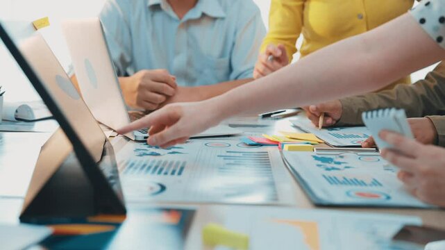 A diverse team engages in a collaborative session, analyzing data and discussing strategies in a modern office setting. Laptops and documents enhance productive communication. SACTR - Powered by Adobe