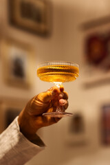 Male hand holds drink in glass  against blurry background. Concept of alcohol, drink, party, degustation, holiday. Copy space for ad.