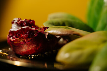 Two juicy halves of a pomegranate are placed on a golden tray on a colored background near a green...