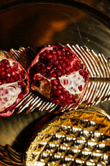 Two juicy halves of a pomegranate are placed on a golden tray on a colored background near a green branch of the plant. A composition for interior decoration and a festive table.