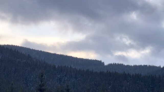 Dramatic clouds rolling over snowy forested mountain range