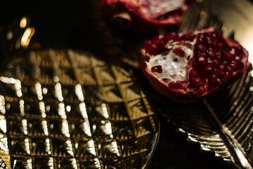 Two juicy halves of a pomegranate are placed on a golden tray on a colored background near a green...