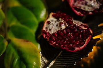 Two juicy halves of a pomegranate are placed on a golden tray on a colored background near a green...