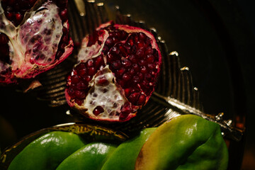 Two juicy halves of a pomegranate are placed on a golden tray on a colored background near a green...