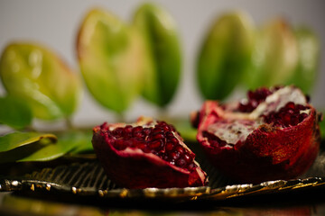 Two juicy halves of a pomegranate are placed on a golden tray on a colored background near a green...