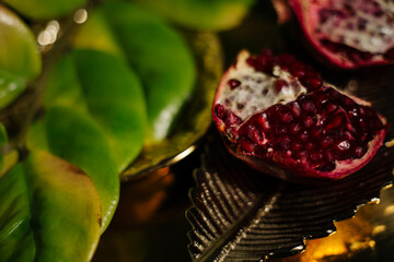Two juicy halves of a pomegranate are placed on a golden tray on a colored background near a green...