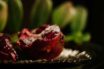 Two juicy halves of a pomegranate are placed on a golden tray on a colored background near a green...