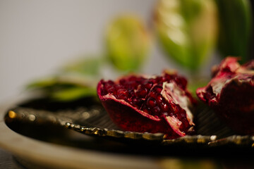 Two juicy halves of a pomegranate are placed on a golden tray on a colored background near a green...