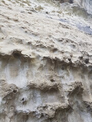Close-up view of a textured rock wall with uneven surfaces and natural erosion patterns. The colors...
