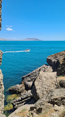 Obraz premium A scenic view of a turquoise sea with a small boat navigating through rocky cliffs under a clear blue sky. The landscape showcases natural beauty and tranquility.