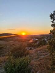 A beautiful sunset over a vast landscape with rolling hills and sparse vegetation. The sky is painted in warm hues of orange and yellow.