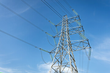 High Voltage Pylon and Power Lines in a Grassy Field Against a Blue Sky