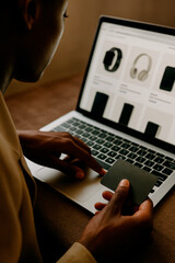 A person making an online purchase of electronic gadgets such as a smartwatch, headphones, and smartphones. The individual is using a laptop in a desk while holding a credit card