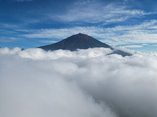 Mountain peak rising above a sea of clouds under a blue sky streaked with thin white clouds