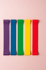 Colorful elastic resistance bands for home exercise. Fitness equipment on light pink background.