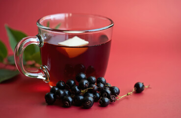 Glass mug filled with dark elderberry tea. Fresh ripe elderberries and green leaves rest beside the cup. Offers natural health benefits and antioxidants for wellness.